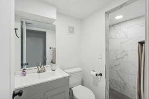 Bathroom featuring a tile shower, vanity, and toilet