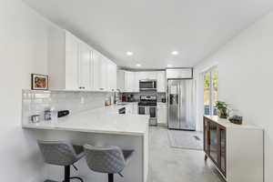 Kitchen with stainless steel appliances, white cabinets, kitchen peninsula, sink, and a breakfast bar area