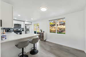 Kitchen with kitchen peninsula, a breakfast bar area, backsplash, white cabinetry, and appliances with stainless steel finishes