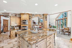 Kitchen featuring a kitchen island, light carpet, a kitchen bar, light stone countertops, and vaulted ceiling