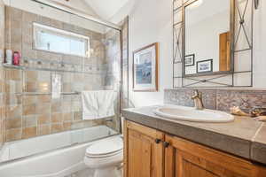 Full bathroom featuring shower / bath combination with glass door, vanity, decorative backsplash, toilet, and lofted ceiling