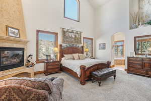 Carpeted bedroom featuring ensuite bathroom, high vaulted ceiling, and a tiled fireplace