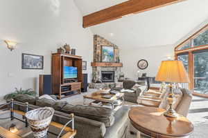 Carpeted living room featuring a stone fireplace, high vaulted ceiling, and beam ceiling