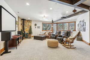 Carpeted home theater with a wood stove and beamed ceiling