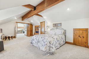 Bedroom with light colored carpet and vaulted ceiling with beams