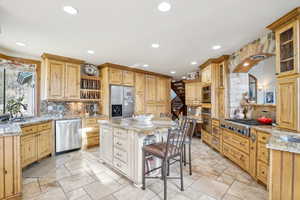 Kitchen with a breakfast bar, a center island, sink, light stone countertops, and appliances with stainless steel finishes