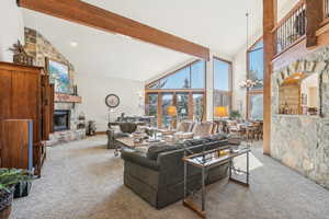 Living room featuring carpet flooring, high vaulted ceiling, beam ceiling, and a stone fireplace