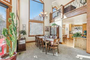 Carpeted dining area featuring a towering ceiling and an inviting chandelier