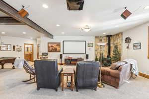 Cinema featuring beamed ceiling, a wood stove, and carpet flooring