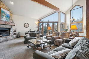 Carpeted living room featuring beam ceiling, a stone fireplace, high vaulted ceiling, and an inviting chandelier