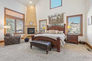 Carpeted bedroom with a towering ceiling, a fireplace, and multiple windows