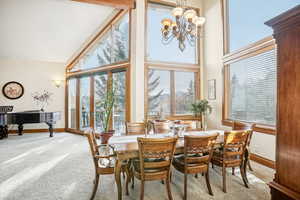 Carpeted dining area featuring high vaulted ceiling, an inviting chandelier, and a wealth of natural light