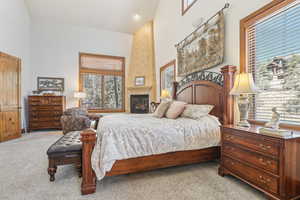 Carpeted bedroom with a large fireplace and high vaulted ceiling