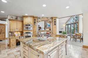 Kitchen featuring light stone countertops, a kitchen bar, stainless steel double oven, light brown cabinets, and a kitchen island