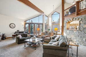 Living room featuring french doors, ceiling fan with notable chandelier, beam ceiling, high vaulted ceiling, and carpet floors