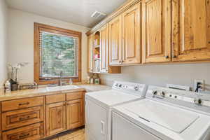 Clothes washing area featuring washing machine and dryer, sink, light tile patterned flooring, and cabinets