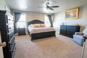 Bedroom featuring multiple windows, a textured ceiling, light carpet, and ceiling fan