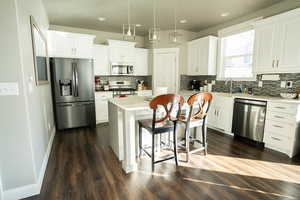 Kitchen with stainless steel appliances, decorative light fixtures, white cabinets, a center island, and dark wood-type flooring