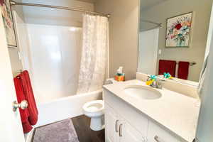 Full bathroom with shower / bath combination with curtain, vanity, hardwood / wood-style flooring, and toilet