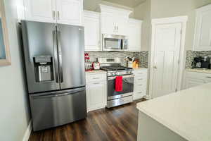 Kitchen featuring white cabinetry, appliances with stainless steel finishes, dark hardwood / wood-style floors, and backsplash