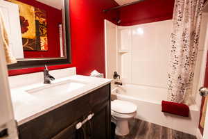 Full bathroom with toilet, shower / tub combo, vanity, and wood-type flooring