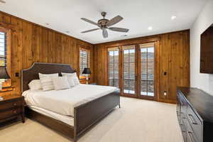 Bedroom with wood walls, french doors, light colored carpet, and ceiling fan