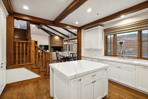 Kitchen with vaulted ceiling with beams, a stone fireplace, white cabinetry, dark hardwood / wood-style floors, and sink