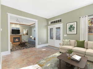 Living room featuring ceiling fan, a glass covered fireplace, baseboards, french doors, and a raised ceiling