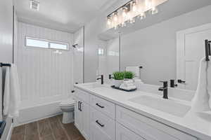 Full bathroom featuring vanity, toilet, tiled shower / bath combo, and a textured ceiling