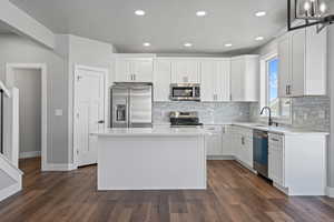 Kitchen featuring dark wood-type flooring, decorative light fixtures, a kitchen island, stainless steel appliances, and white cabinets