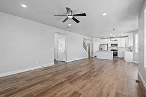 Unfurnished living room with sink, hardwood / wood-style flooring, ceiling fan with notable chandelier, and a textured ceiling