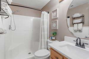 Bathroom with toilet, a shower with curtain, vanity, and a textured ceiling