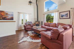 Living room featuring dark wood-type flooring, a wealth of natural light, a wood stove, and a towering ceiling