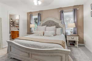 Bedroom with ensuite bathroom, ceiling fan, and light carpet