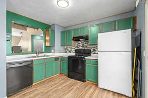 Kitchen featuring light wood-type flooring, black appliances, sink, and tasteful backsplash