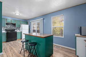 Kitchen featuring black range with electric cooktop, a wealth of natural light, a breakfast bar area, and white refrigerator