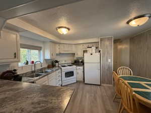 Kitchen with light hardwood / wood-style floors, sink, white appliances, a textured ceiling, and white cabinets