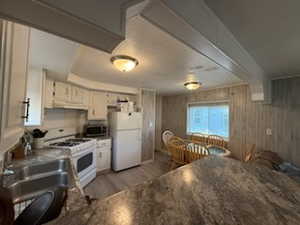 Kitchen with white cabinetry, wooden walls, white appliances, light stone counters, and sink