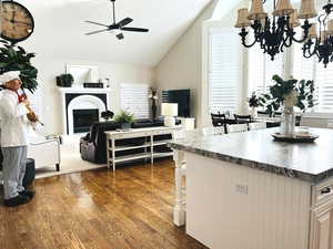 Kitchen featuring a breakfast bar, white cabinetry, ceiling fan with notable chandelier, vaulted ceiling, and dark hardwood / wood-style floors