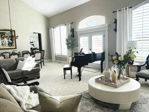 Carpeted living room with a healthy amount of sunlight, high vaulted ceiling, and french doors