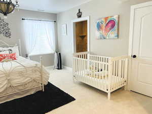 Bedroom featuring a chandelier, a nursery area, and light carpet