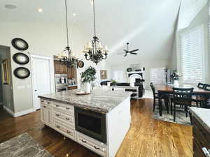 Kitchen with stainless steel appliances, dark hardwood / wood-style flooring, light stone counters, ceiling fan with notable chandelier, and a center island