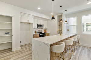 Kitchen with white cabinetry, decorative light fixtures, appliances with stainless steel finishes, kitchen peninsula, and light stone countertops