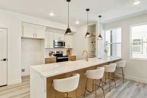 Kitchen featuring appliances with stainless steel finishes, white cabinetry, sink, hanging light fixtures, and light stone counters