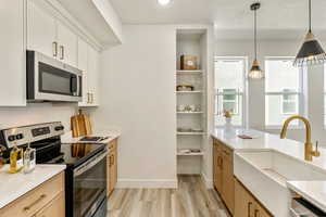 Kitchen with sink, decorative light fixtures, light wood-type flooring, stainless steel appliances, and white cabinets