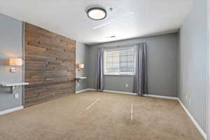 Unfurnished Main Bedroom room with an accent wall, light carpet, wooden walls, a textured ceiling, and baseboards