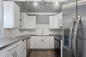 Kitchen with dark wood-style flooring, a sink, white cabinetry, appliances with stainless steel finishes, and backsplash