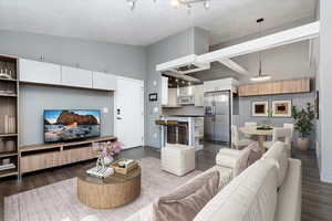 FURNISHED Living Room area with a textured ceiling, high vaulted ceiling, dark wood-style flooring, and baseboards