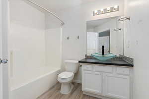 Full bathroom with bathing tub / shower combination, vanity, toilet, and wood finished floors