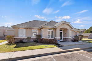 View of front facade featuring stone siding, a shingled roof, a front lawn, and stucco siding